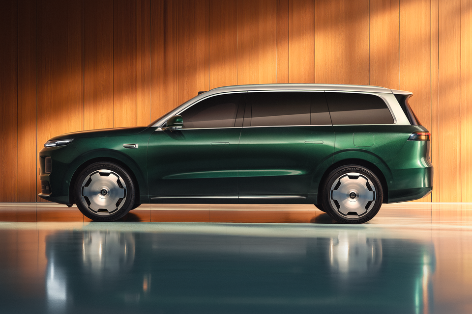 Um SUV grande Leapmotor D19 verde com teto prateado, visto de lado e estacionado em frente a uma parede com painéis de madeira