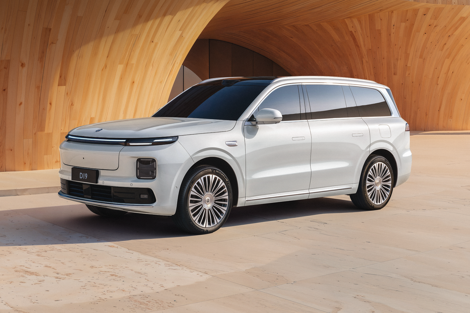 Um grande SUV Leapmotor D19 branco estacionado em frente a uma parede curva de madeira, visto de um ângulo frontal de três quartos