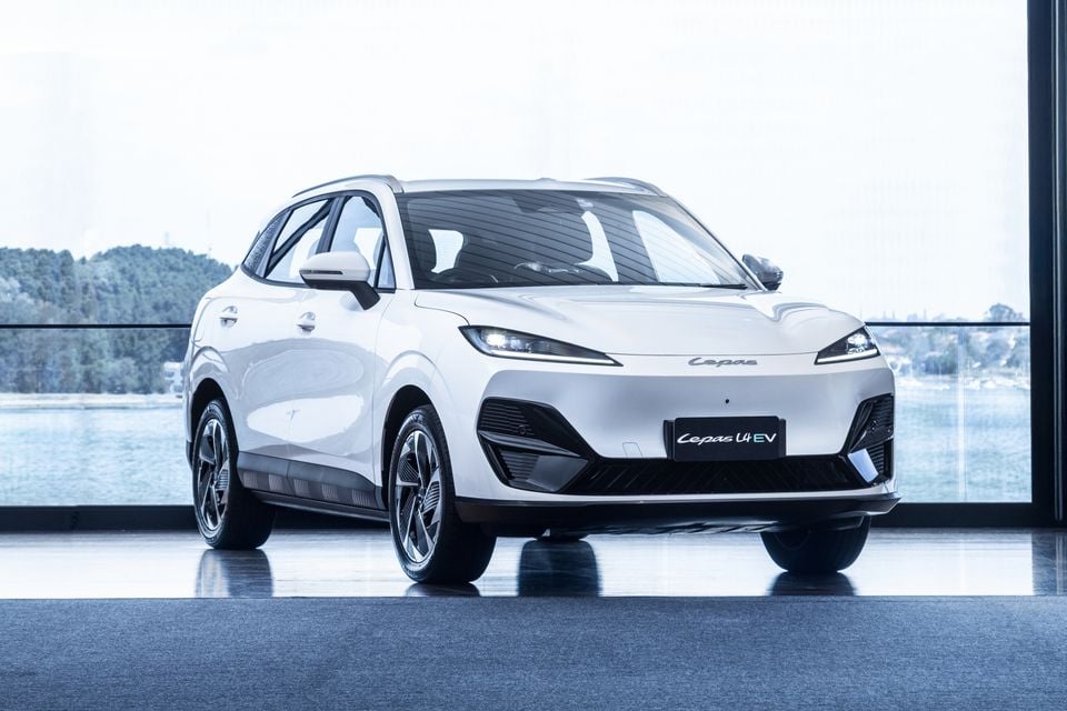 A white Cepas U4 EV electric SUV seen from the front-side angle, displayed indoors with a waterfront view in the background.