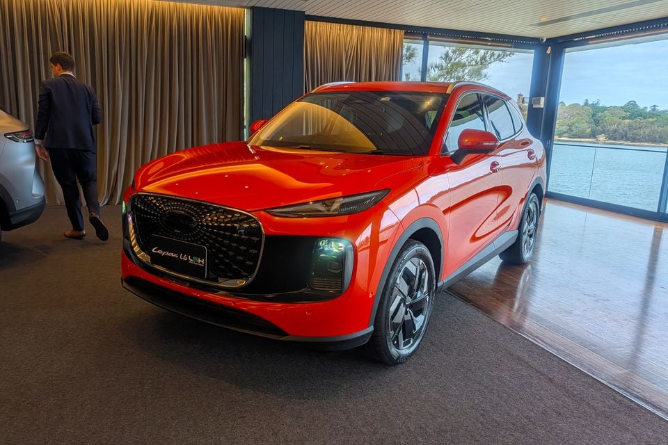 A red Lepas L6 LSH SUV displayed indoors at a media event, seen from the front-left angle