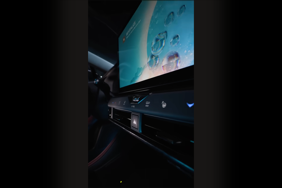 Close-up of a car's large touchscreen infotainment display and centre console controls, seen from the rear seat area, likely a Lexus NX teaser