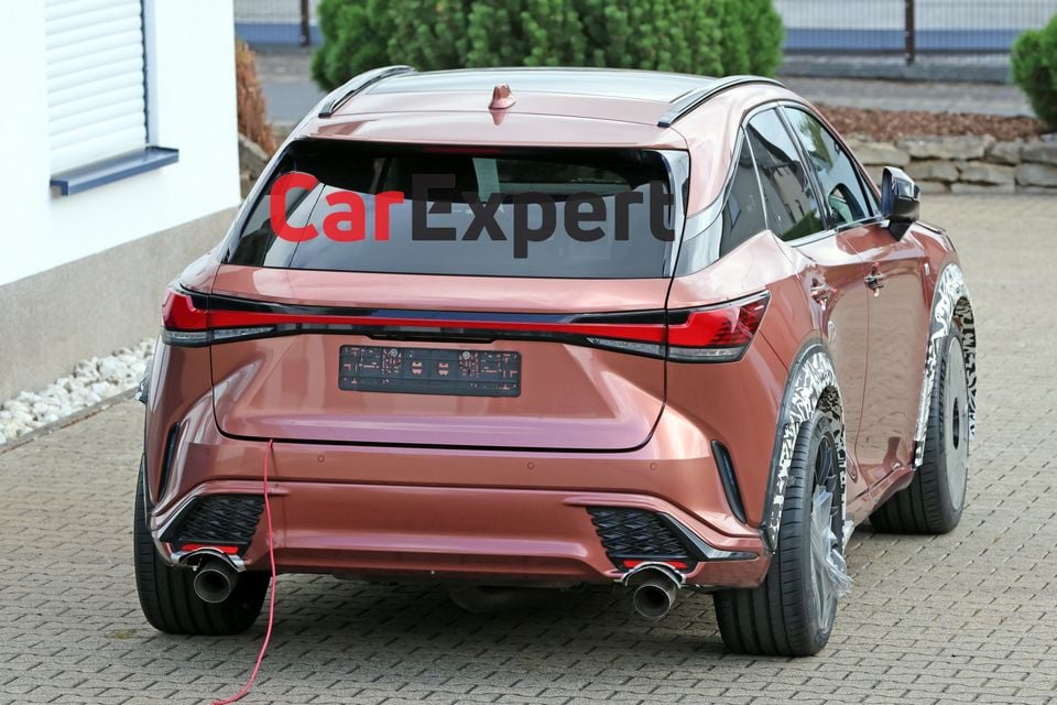 Rear view of a bronze Lexus RX Morizo RR prototype on a cobblestone driveway, showing quad exhaust tips and partially camouflaged rear wheels