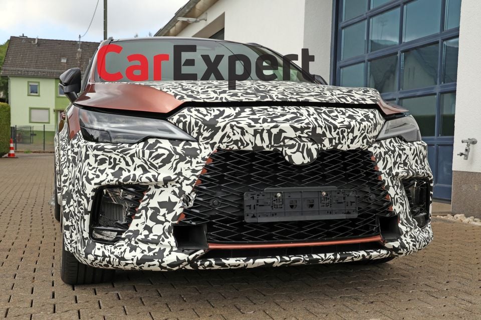 A camouflaged Lexus RX Morizo RR prototype seen from the front, showing an aggressive grille and splitter with copper accents