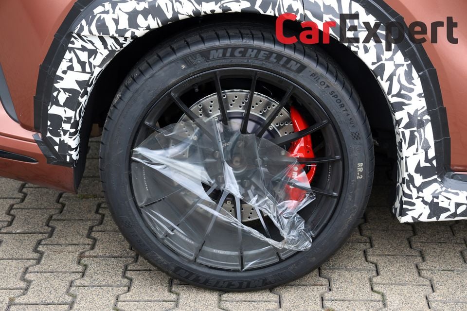 Close-up of a camouflaged prototype vehicle's wheel, showing a large alloy rim with red brake calipers and Michelin Pilot Sport 4 SUV tyres, with the wheel centre wrapped in protective plastic