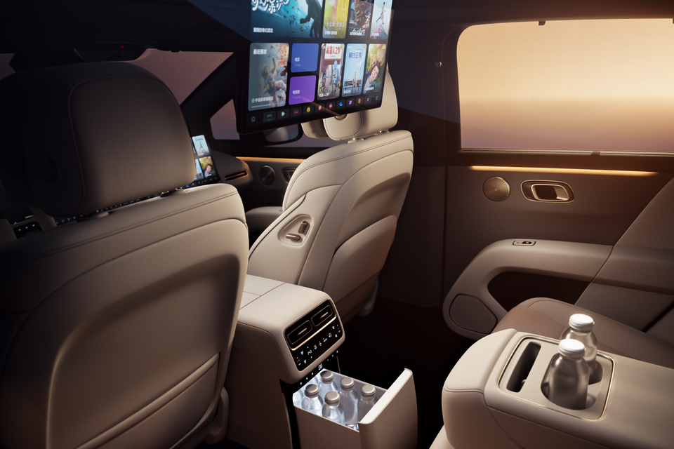 Luxurious rear cabin interior of a Li Auto i6 showing cream leather seats, a large rear entertainment screen, rear climate controls, a built-in mini fridge with bottles, and a water bottle in the centre console cup holder