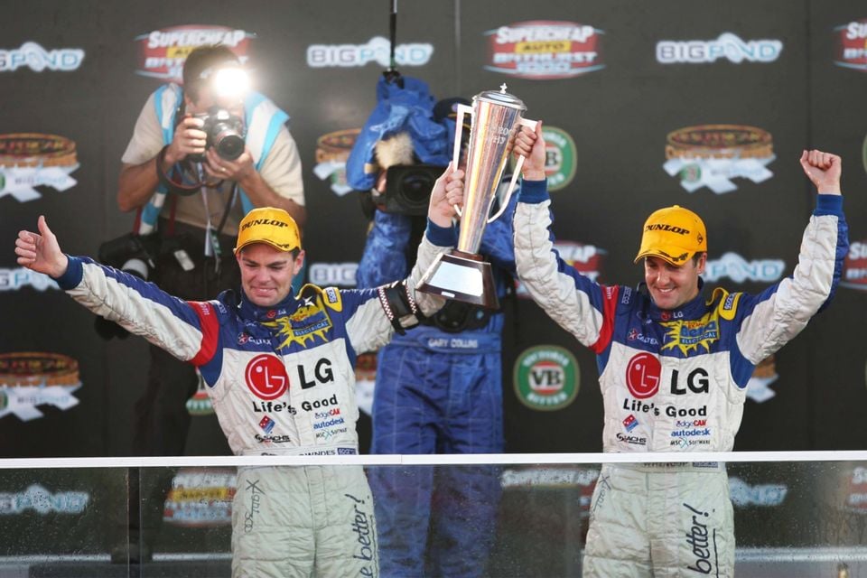 Craig Lowndes and Jamie Whincup celebrate on the podium at the 2006 Bathurst 1000, holding a trophy aloft in LG-sponsored race suits