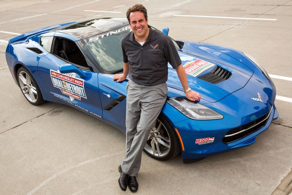 Mark Reuss leaning on a blue Chevrolet Corvette Stingray coupe, the official pace car for the Chevrolet Indy Dual in Detroit, parked on concrete