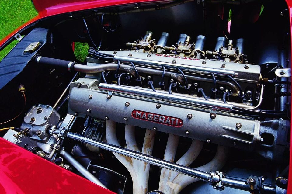 The exposed inline six-cylinder engine of a red classic Maserati A6GCS, with a Maserati-branded cam cover, carburettors and exhaust headers