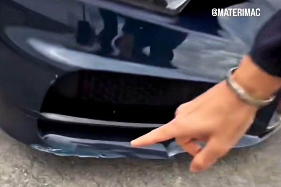 A person points to scrapes and damage on the lower front bumper and air intake of a dark blue Bugatti Chiron
