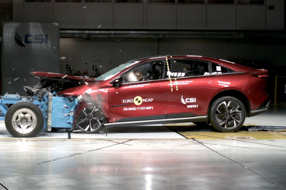 A red Mazda 6e sedan undergoing a Euro NCAP frontal crash test, with significant front-end damage visible after impact with the barrier.