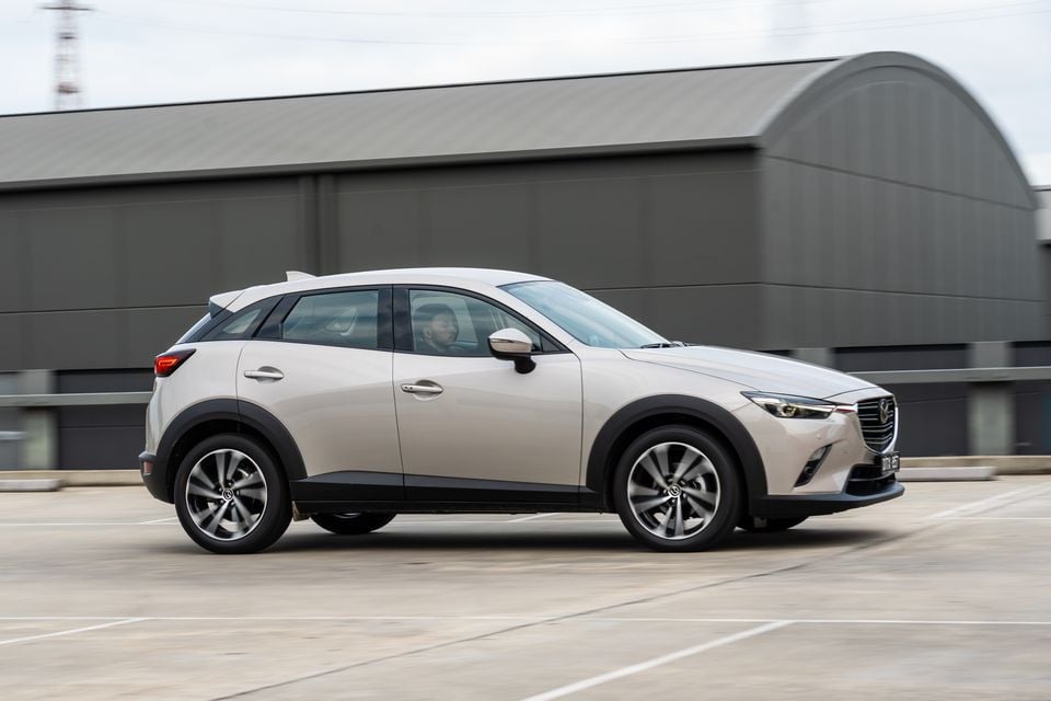 A white Mazda CX-3 small SUV seen from the side while driving through a car park
