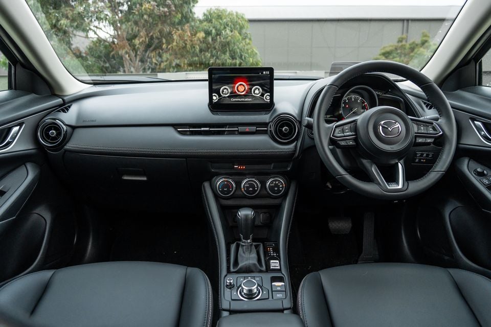 Mazda CX-3 interior showing the dashboard, central infotainment touchscreen displaying the Communication menu, steering wheel, automatic gear shifter, and climate controls on a right-hand drive layout