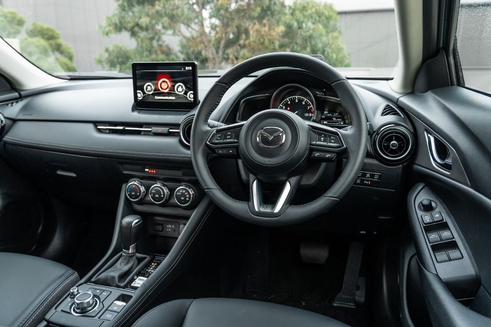 Mazda CX-3 interior showing the steering wheel, dashboard, infotainment screen and centre console from the driver's seat perspective