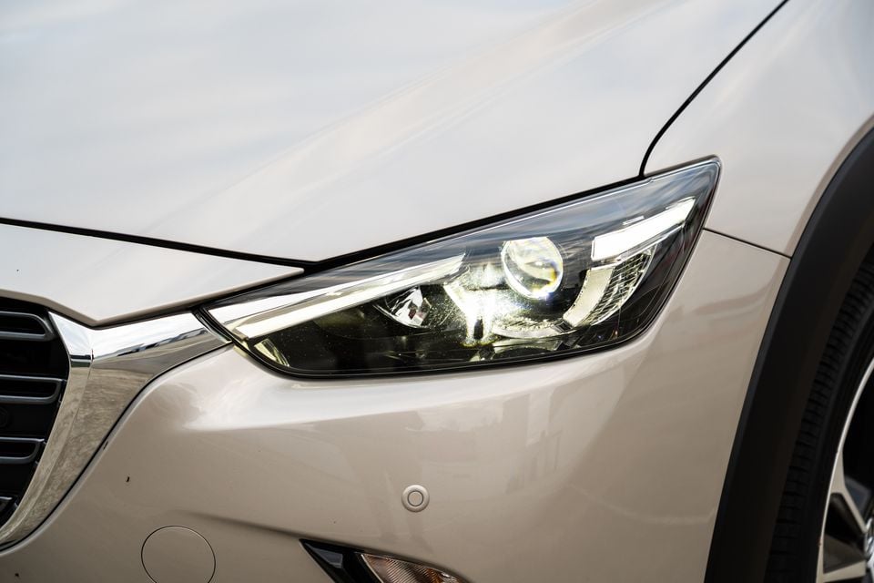 Close-up of the front headlight on a beige Mazda CX-3, showing its slim LED daytime running light design