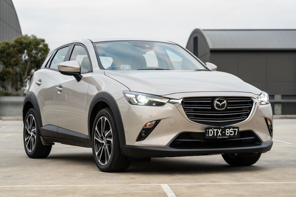A champagne Mazda CX-3 small SUV seen from the front-side angle in a car park