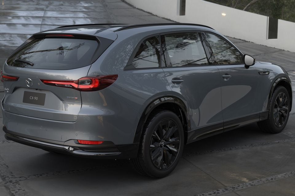 A grey Mazda CX-90 SUV seen from the rear three-quarter angle, showing its tail lights, black alloy wheels, and CX-90 badging