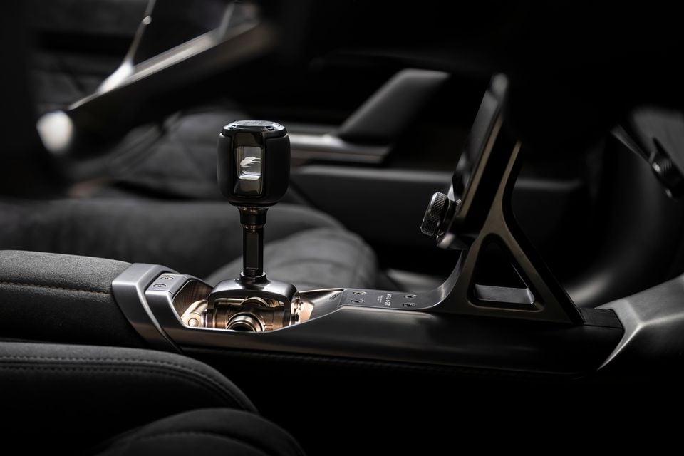 Close-up of the gear selector and centre console inside a McLaren, featuring an intricate mechanical shifter mechanism with a dark and metallic finish