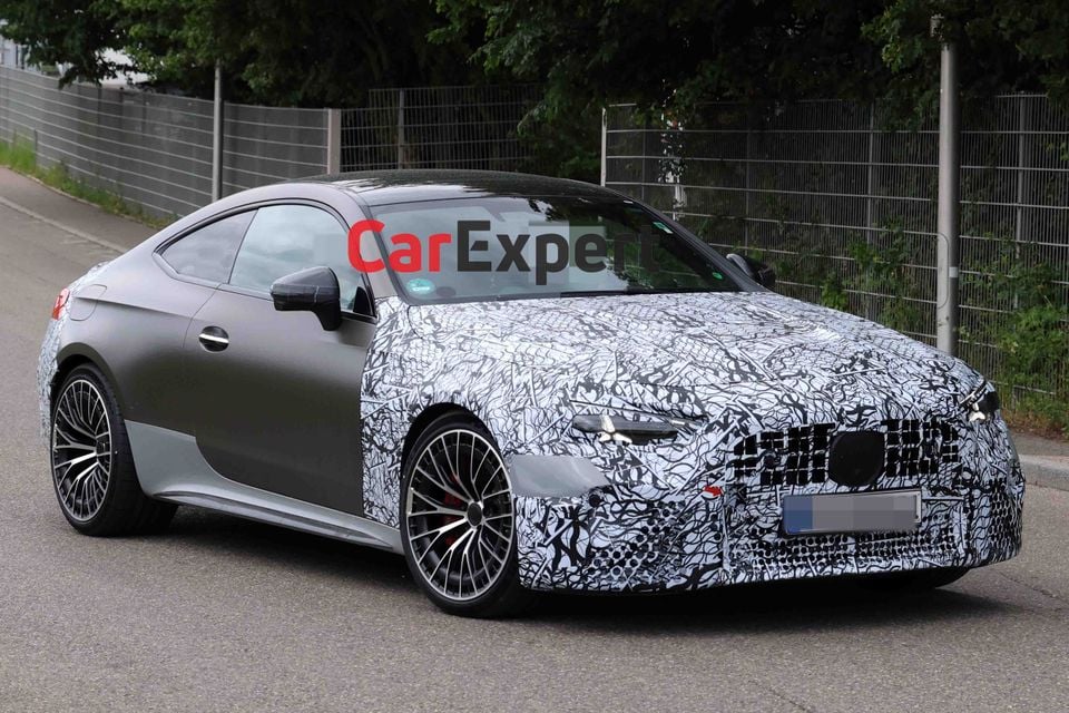 A Mercedes-AMG CLE63 coupe prototype with heavy camouflage wrap on the front and bonnet, seen from the front-side angle on a public road
