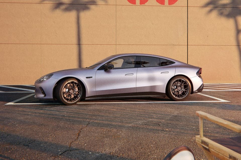 A silver Mercedes-AMG GT 53 4-door coupe seen from the side, parked in a car park with palm tree shadows on a wall behind it