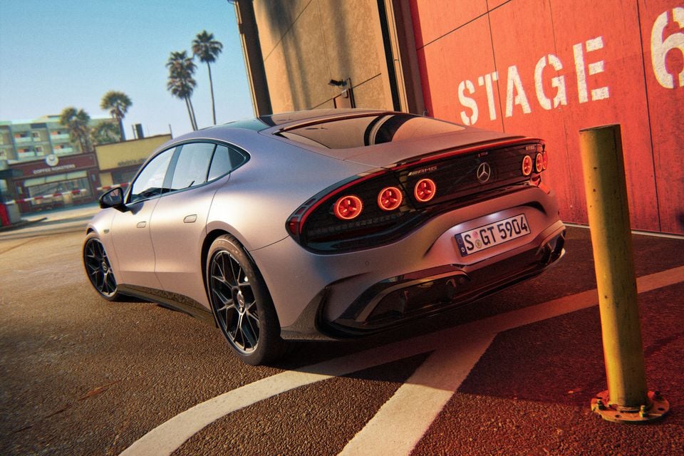 A silver Mercedes-AMG GT 53 four-door coupe seen from the rear three-quarter angle, parked near a red building with palm trees in the background
