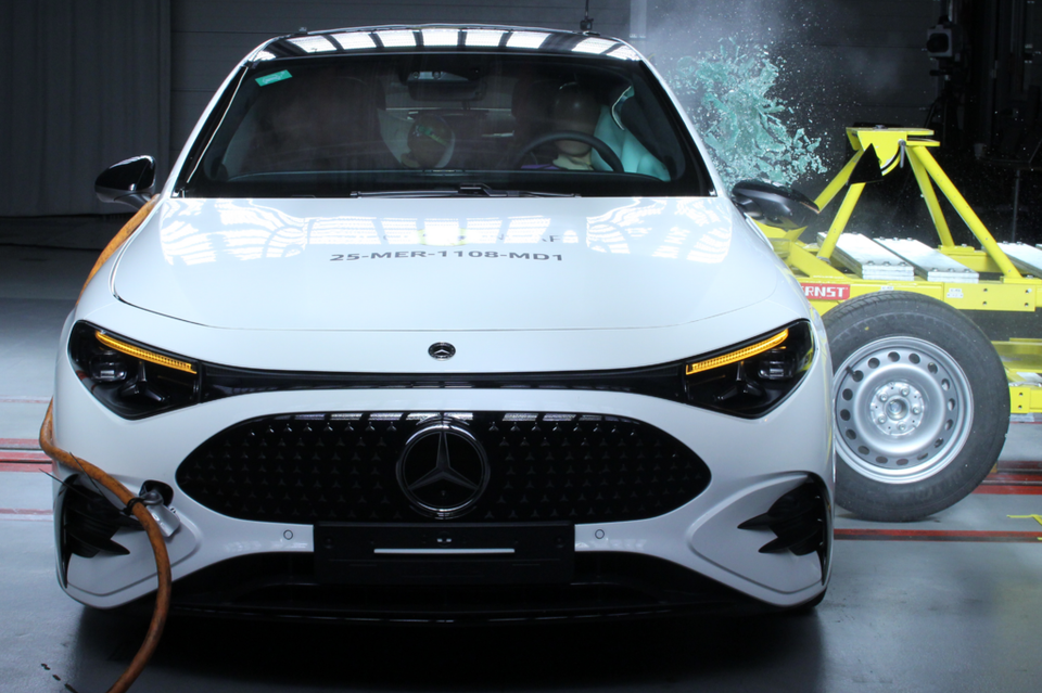 A white Mercedes-Benz CLA seen from the front during a side impact crash test, with a yellow barrier making contact with the passenger side.