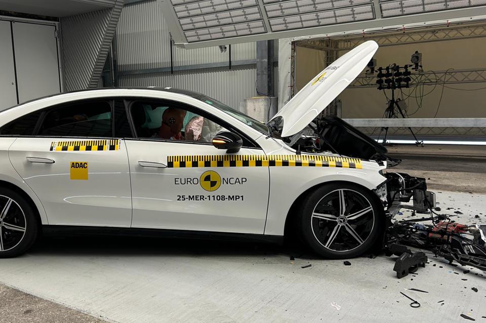 A white Mercedes-Benz CLA after a Euro NCAP frontal crash test, with the bonnet open and front end severely damaged, airbags deployed inside the cabin