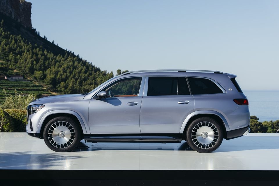 A silver Mercedes-Maybach GLS 680 large luxury SUV seen from the side, parked against a scenic coastal and mountain backdrop