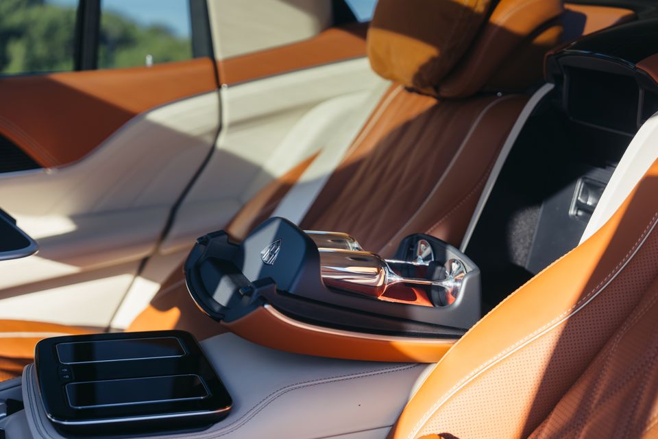 Close-up of the luxury rear centre console area in a Mercedes-Maybach GLS 680, showing a crystal champagne flute holder with glasses and two-tone tan and cream leather upholstery