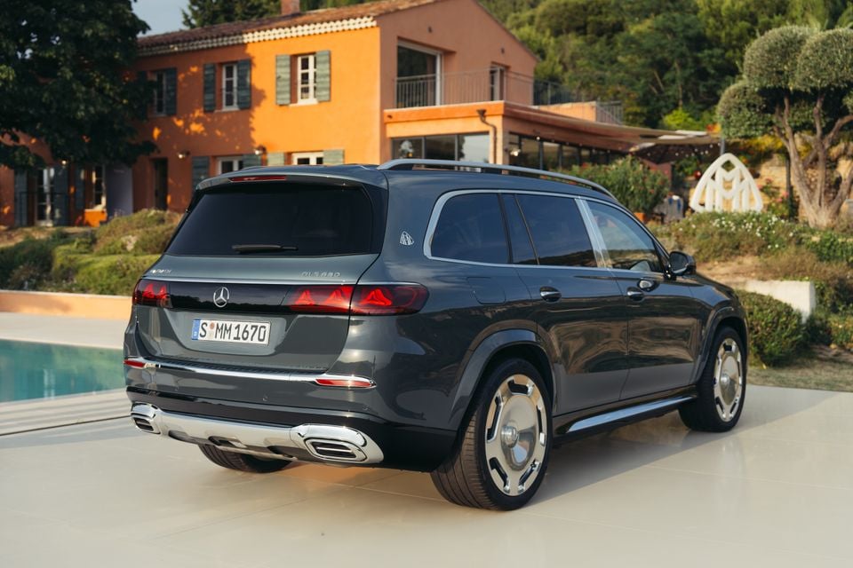 A dark grey Mercedes-Maybach GLS 680 large SUV seen from the rear three-quarter angle, parked outside a villa near a pool