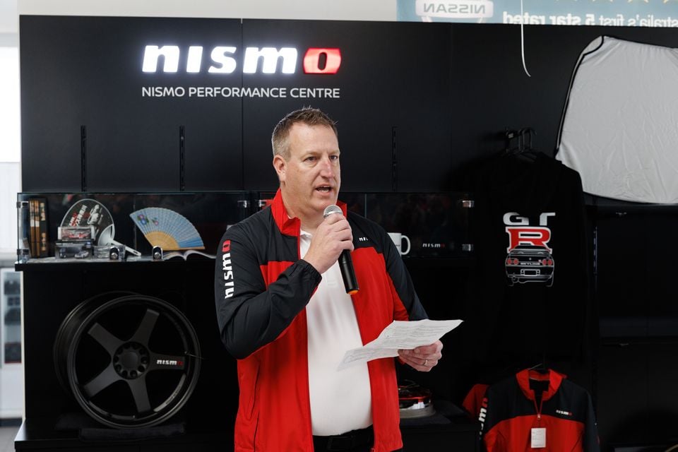 A man in a Nismo jacket speaks into a microphone at the Nissan Nismo Performance Centre, holding notes in his other hand