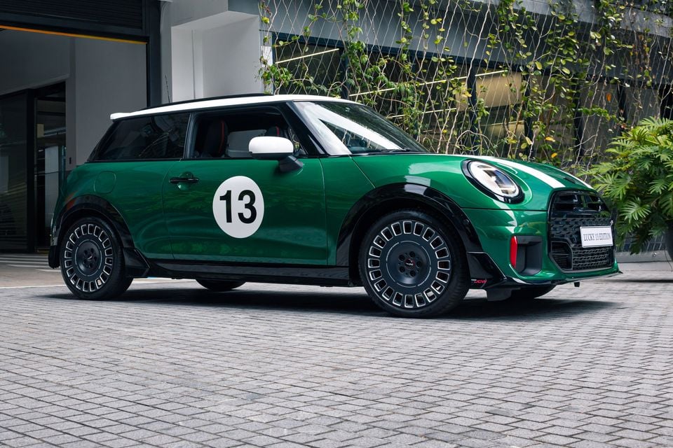 A green Mini Cooper Lucky 13 Edition three-door hatch with a white roof and number 13 roundel, parked on cobblestones, seen from the front side