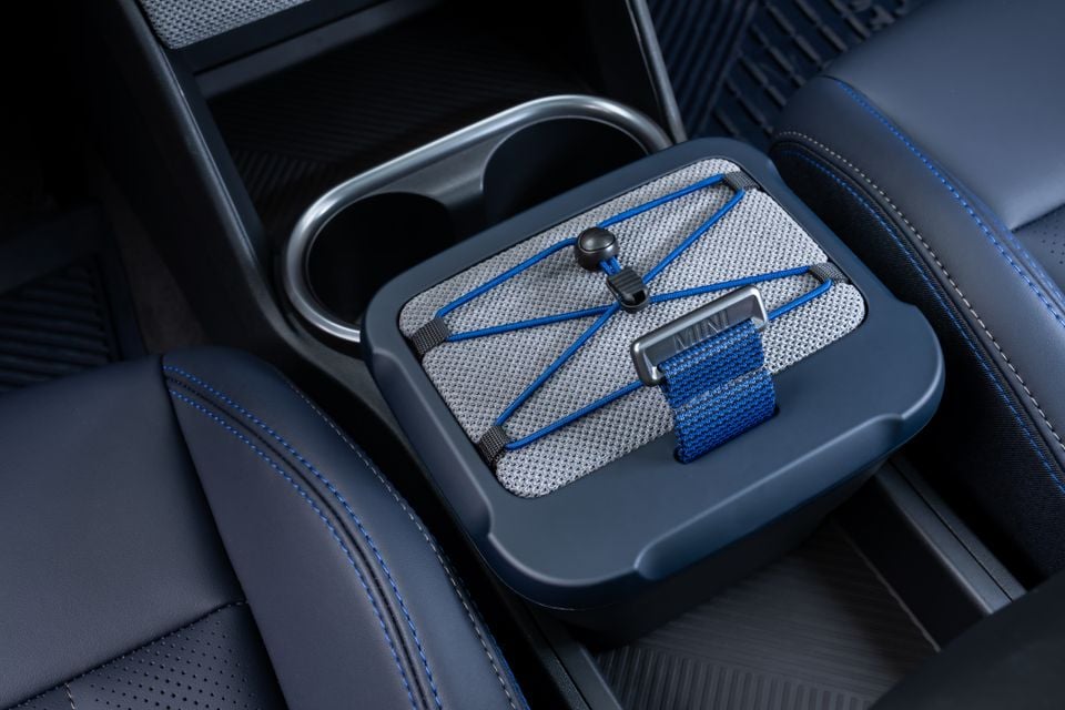A close-up of a storage box with a MINI-branded elastic strap system fitted into the centre console cupholder area of a Mini Countryman Untamed Edition.