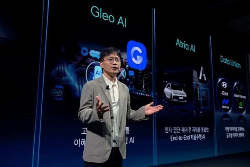 A presenter speaks on stage in front of large screens displaying Hyundai's Gleo AI, Atria AI, and Data Union automotive AI platform concepts