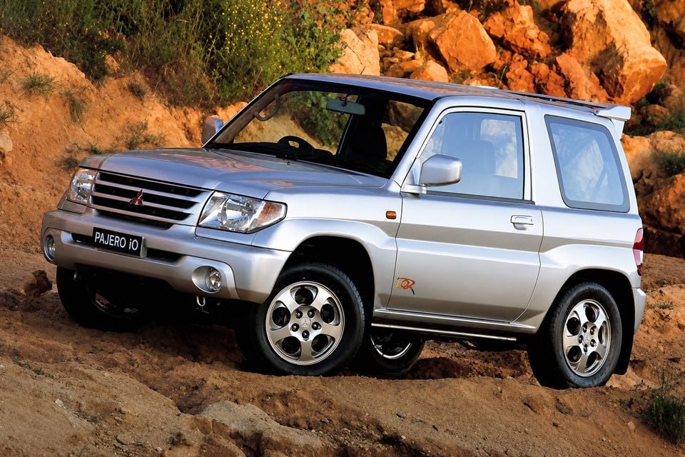 A silver Mitsubishi Pajero iO short-wheelbase SUV seen from the front-side angle, parked on rocky terrain outdoors.