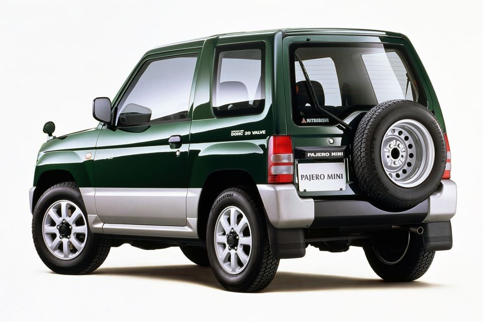A green Mitsubishi Pajero Mini small SUV seen from the rear three-quarter angle, showing a rear-mounted spare wheel, on a white background.