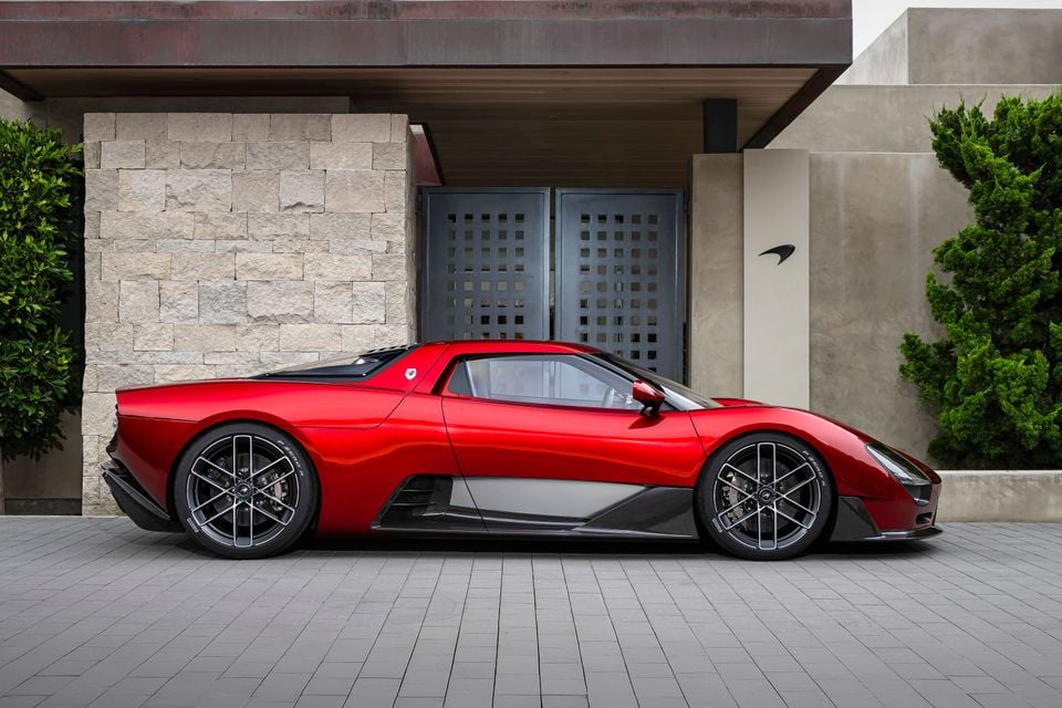 A red Czinger Monterey P50 supercar seen from the side, parked outside a modern building
