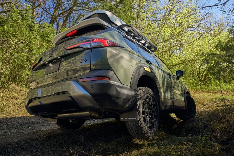 A green 2028 Mitsubishi Outlander Diamond Trail Edition concept with a roof rack and all-terrain tyres, parked on a grassy trail and seen from the low rear