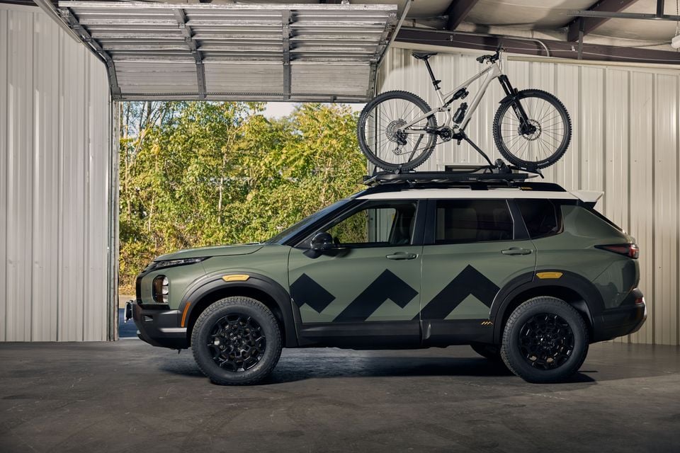 Green 2028 Mitsubishi Outlander Diamond Trail Edition SUV with black chevron graphics and a mountain bike on its roof rack, parked in a garage