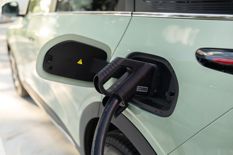 A charging cable plugged into the charge port of a light green Geely EX2 electric vehicle