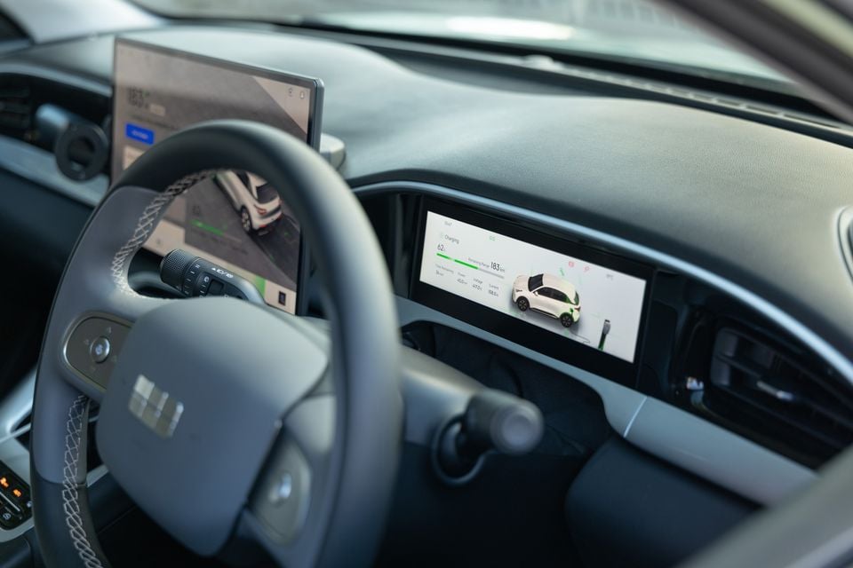 Interior of a Geely EX2 showing the steering wheel and dual screens displaying a charging status screen with 183km remaining range and a bird's-eye camera view