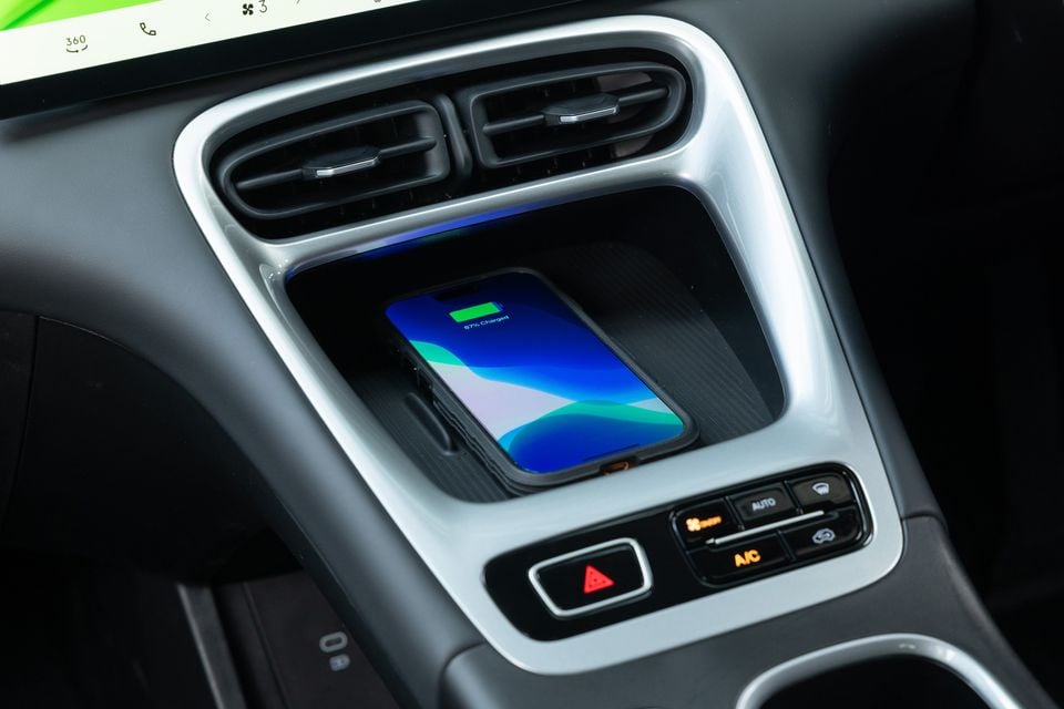 A smartphone wirelessly charging in the centre console of a Geely EX2, with climate control buttons visible below