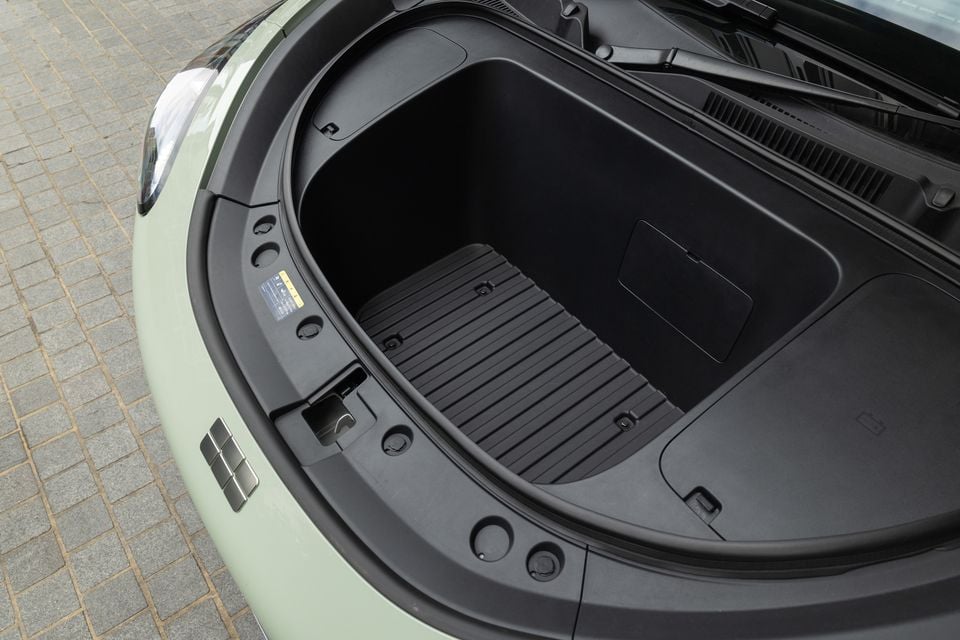 Open frunk (front boot) of a light green Geely EX2 electric vehicle, showing the empty storage compartment with a rubberised mat, viewed from above
