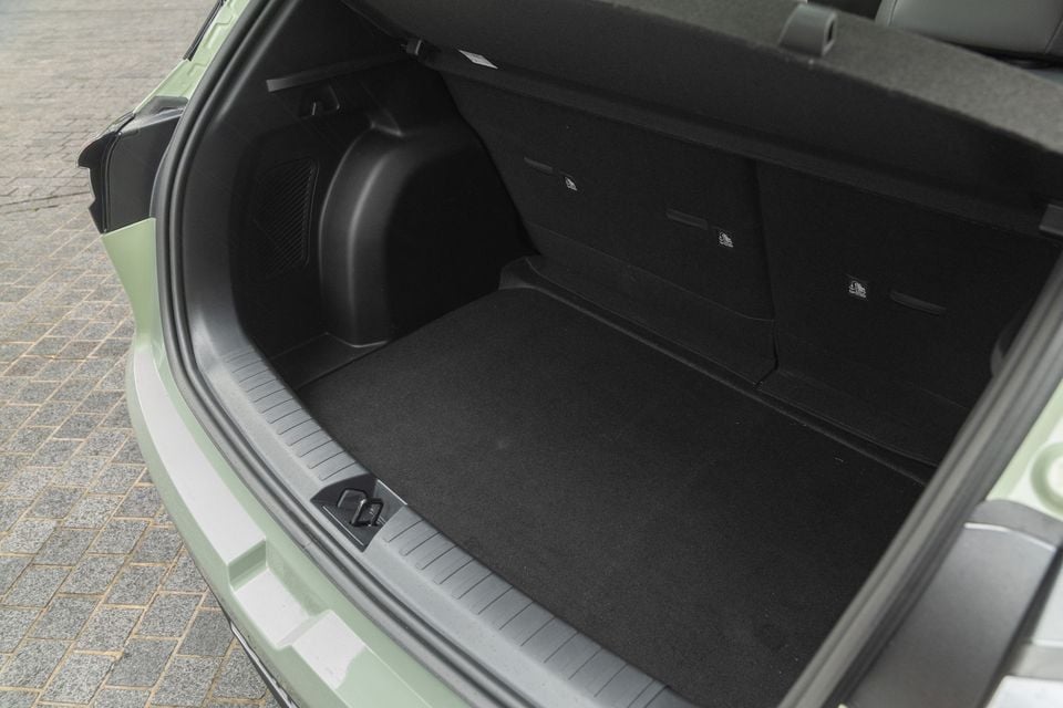 The open boot of a light green Geely EX2, showing a flat, carpeted load floor with a rear seatback fold lever and plastic wheel arch intrusion on the left side.