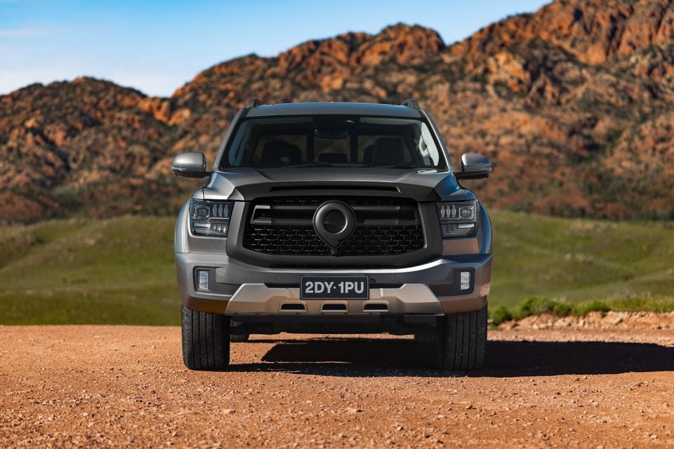 A grey GWM Cannon Alpha large SUV seen from the front, parked on a dirt road with rocky hills in the background.