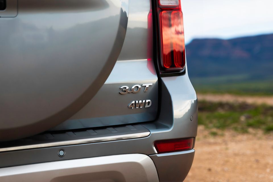 Close-up of the rear of a GWM Tank 500 SUV showing the 3.0T and 4WD badges, tail light, and spare wheel cover, with an outdoor landscape in the background