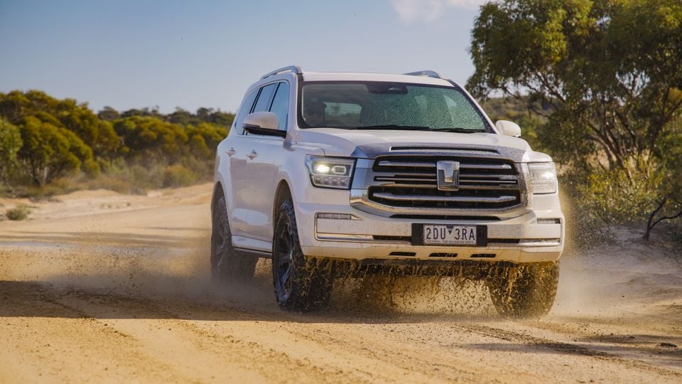 A white GWM Tank 500 SUV driving on a dusty outback dirt track, seen from the front