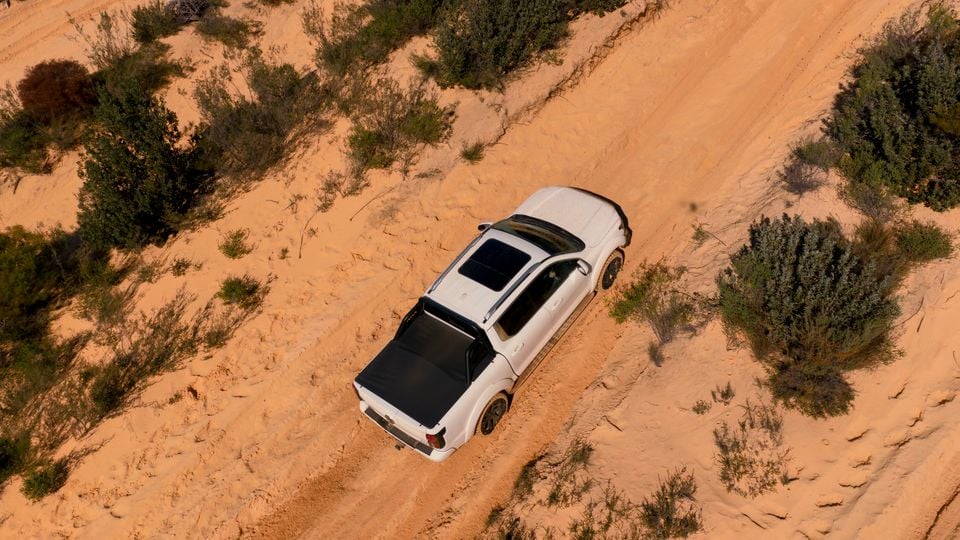 A white GWM Tank 500 ute seen from above driving along a sandy outback track, surrounded by scrubland