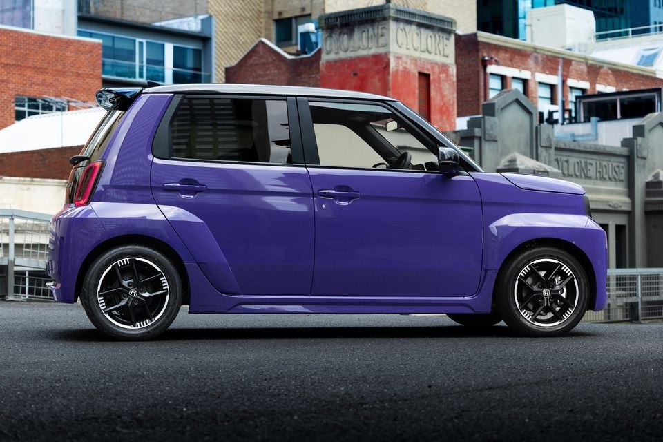A purple Honda Super One compact hatchback seen from the side, parked on a street in front of urban brick buildings