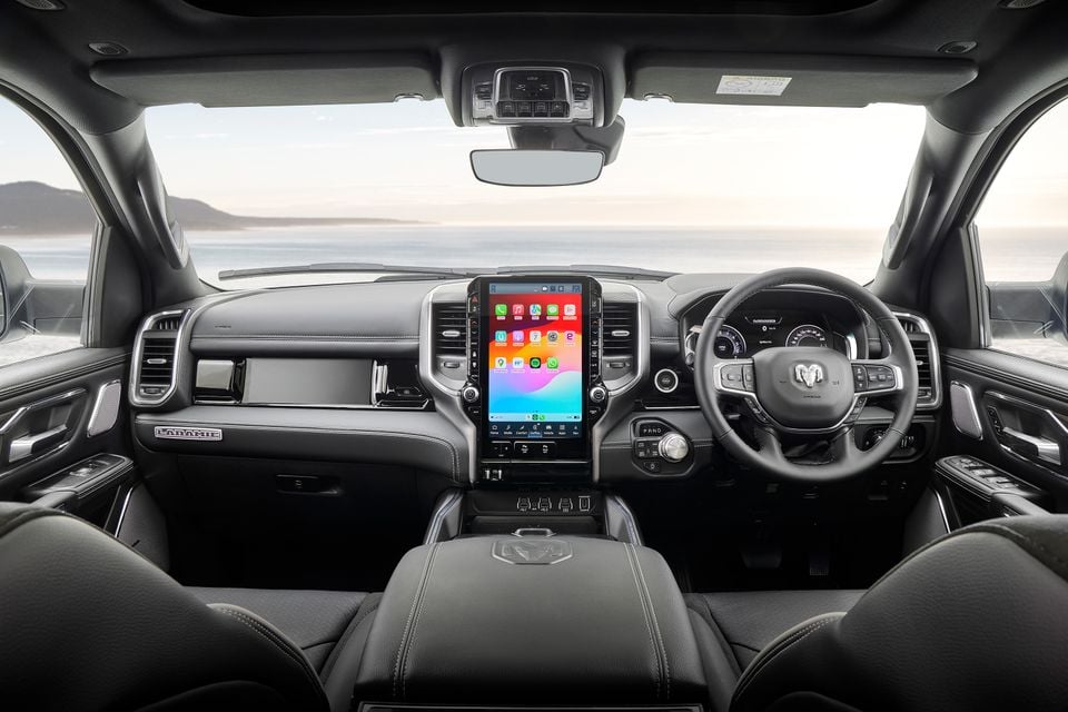 Interior dashboard view of a Ram 1500 Laramie, featuring a large vertical touchscreen with Apple CarPlay, leather seats, and right-hand drive layout