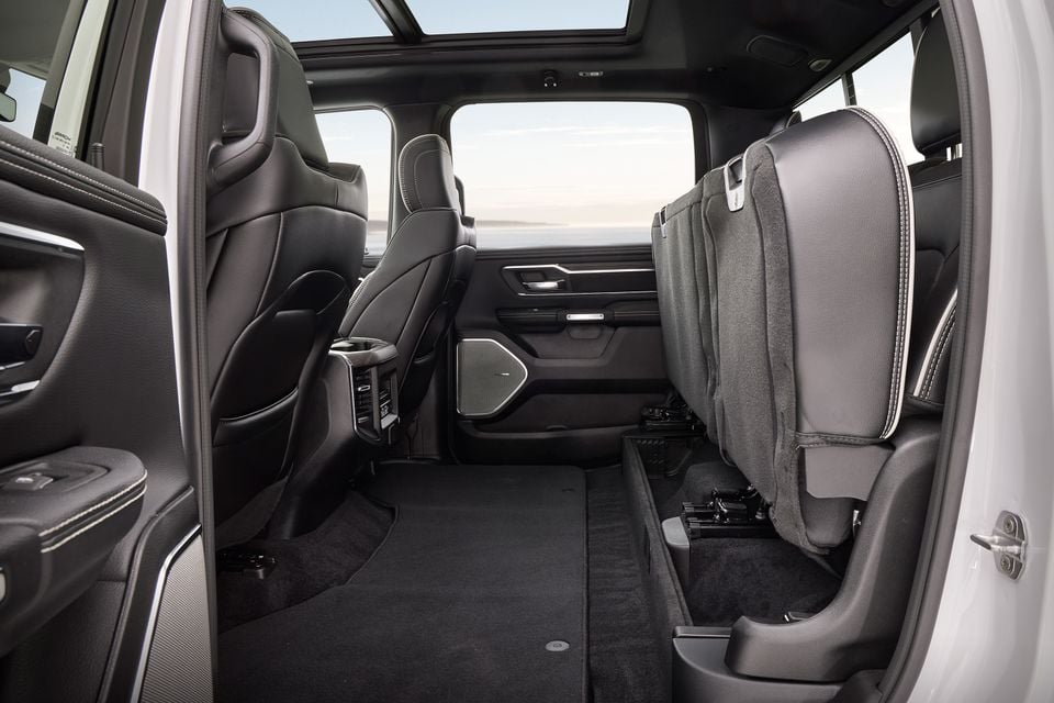 Interior rear seat area of a Ram 1500 Laramie Night Edition showing folded rear seats with black leather upholstery, rear climate controls, speakers, and a panoramic sunroof overhead